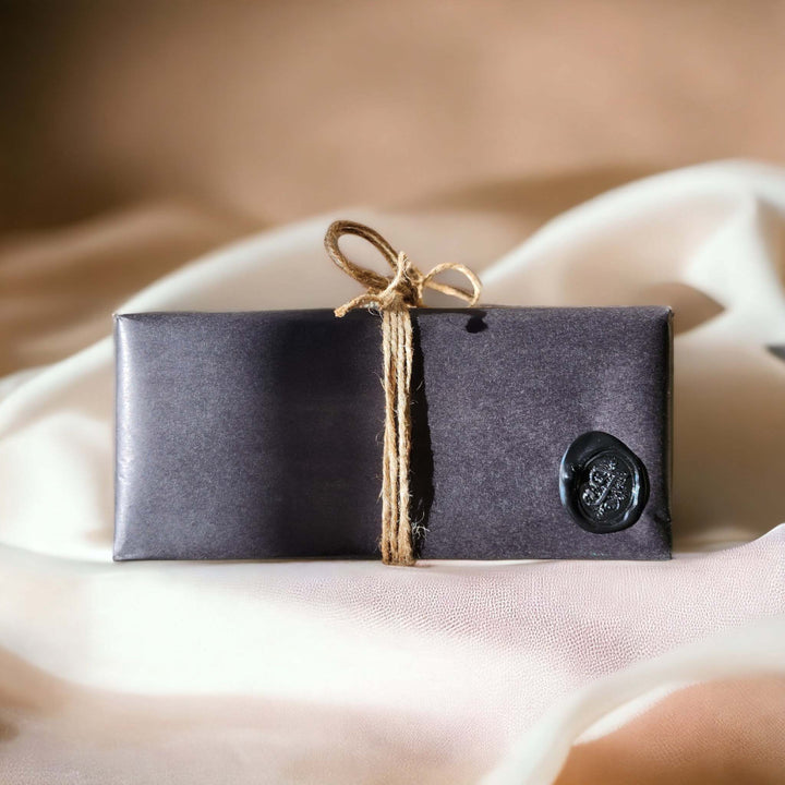 Luxury candle gift set by Alchemy & Aura wrapped with natural twine in black kraft paper. Side view with wax seal stamp.