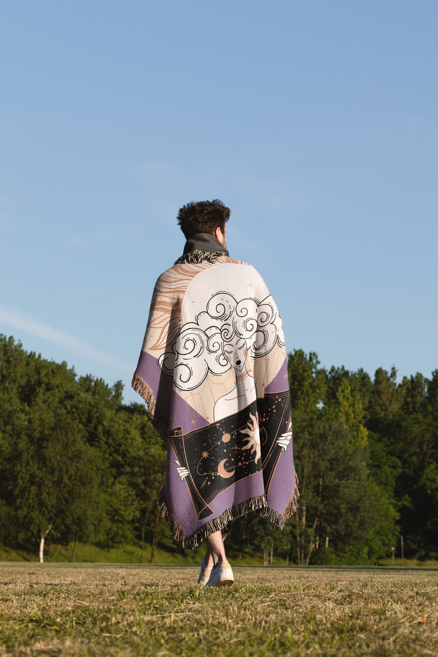 Woven blanket with spiritual themes, a woman with her head in clouds holding a scroll of the sun. Draped over the shoulders of a man standing in a field of gass. 